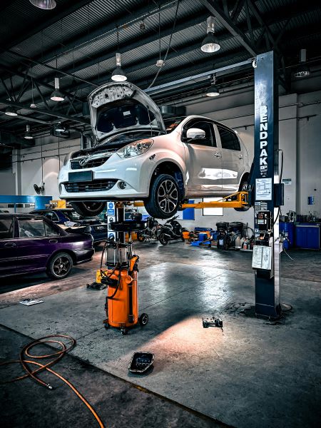 A white car on a vehicle lift and undergoing maintenance in a workshop