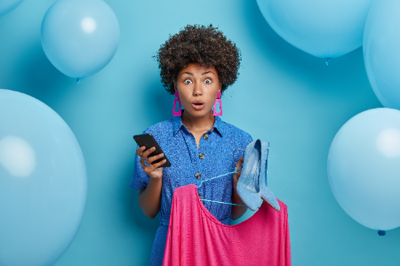 emotive-scared-woman-stylish-clothes-chooses-dress-high-heel-shoes-dress-birthday-party-holds-smartphone