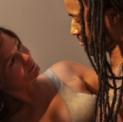 A man with locs and a woman sitting on a bed and having an intimate discussion