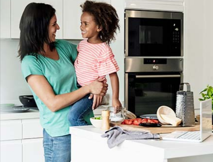 A woman holding a young girl in a kitchen and both smiling