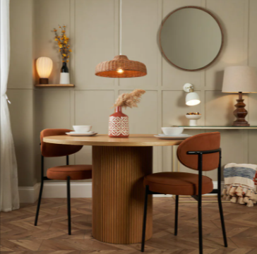 A round wooden table with white bowls and plates and two brown chairs