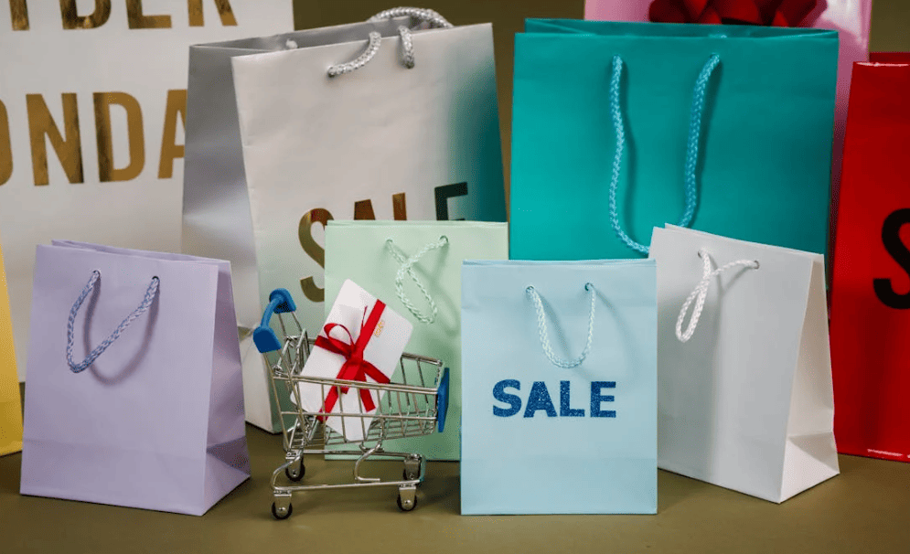A mix of colourful shopping bags and a mini novelty shopping cart with a debit card wrapped in a bow on a table with a brown background