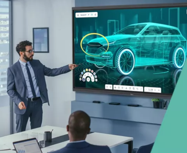 A man dressed in a suit standing beside a large screen discpaying a car