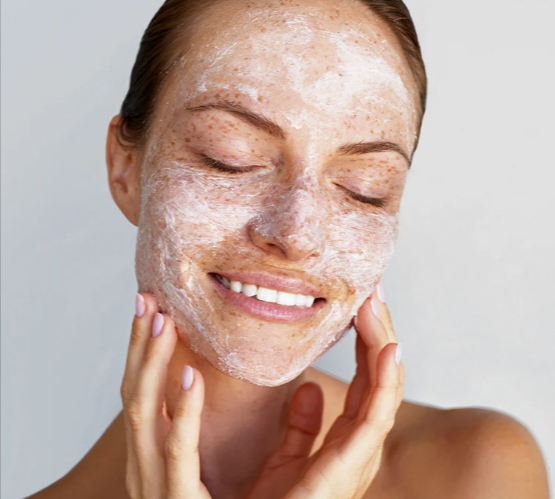 A woman with closed eyes smiling while applying a foamy cleanser on her face