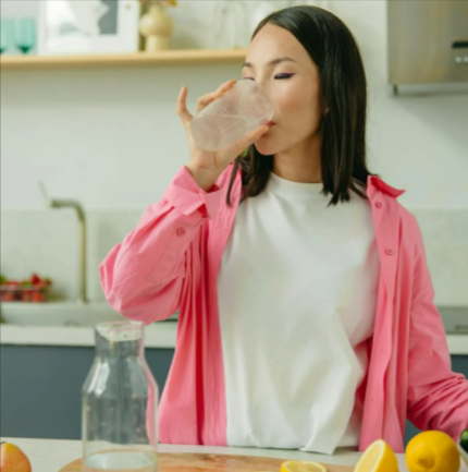 A woman in a pink overshirt drinking water from a glass