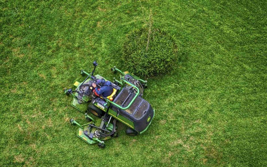 A green and black ride on lawn mower trimming green lawn
