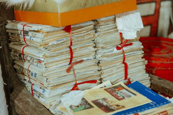 A stack of old newspapers and documents tied with a red string and placed on a wooden surface