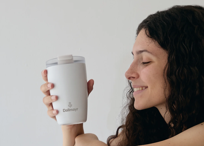 Eine Frau, die lächelnd einen FLSK Becher vor sich hält