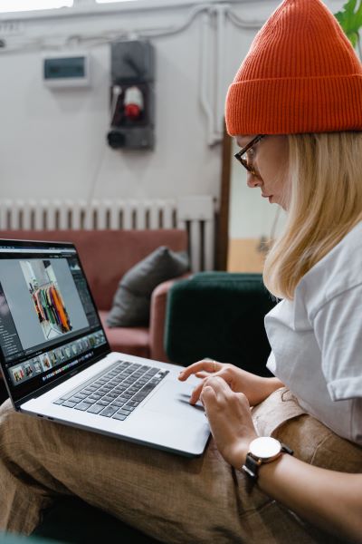 A woman wearing a white t-shirt and an orange beanie working on a laptop