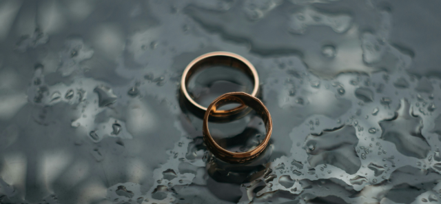 Two wedding bands are placed on a dark wooden table
